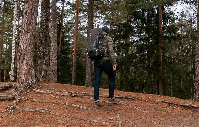 A man in blue jeans hiking in a forest with a hiking backpack