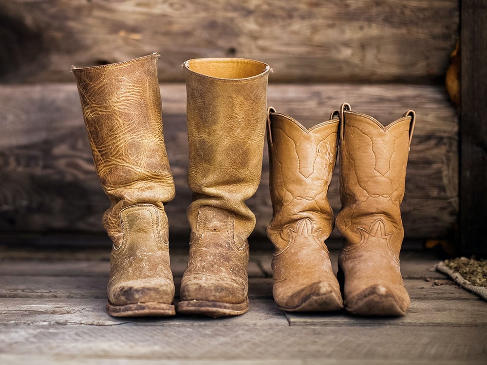 Two pairs of empty cowboy boots male and female on wooden floor